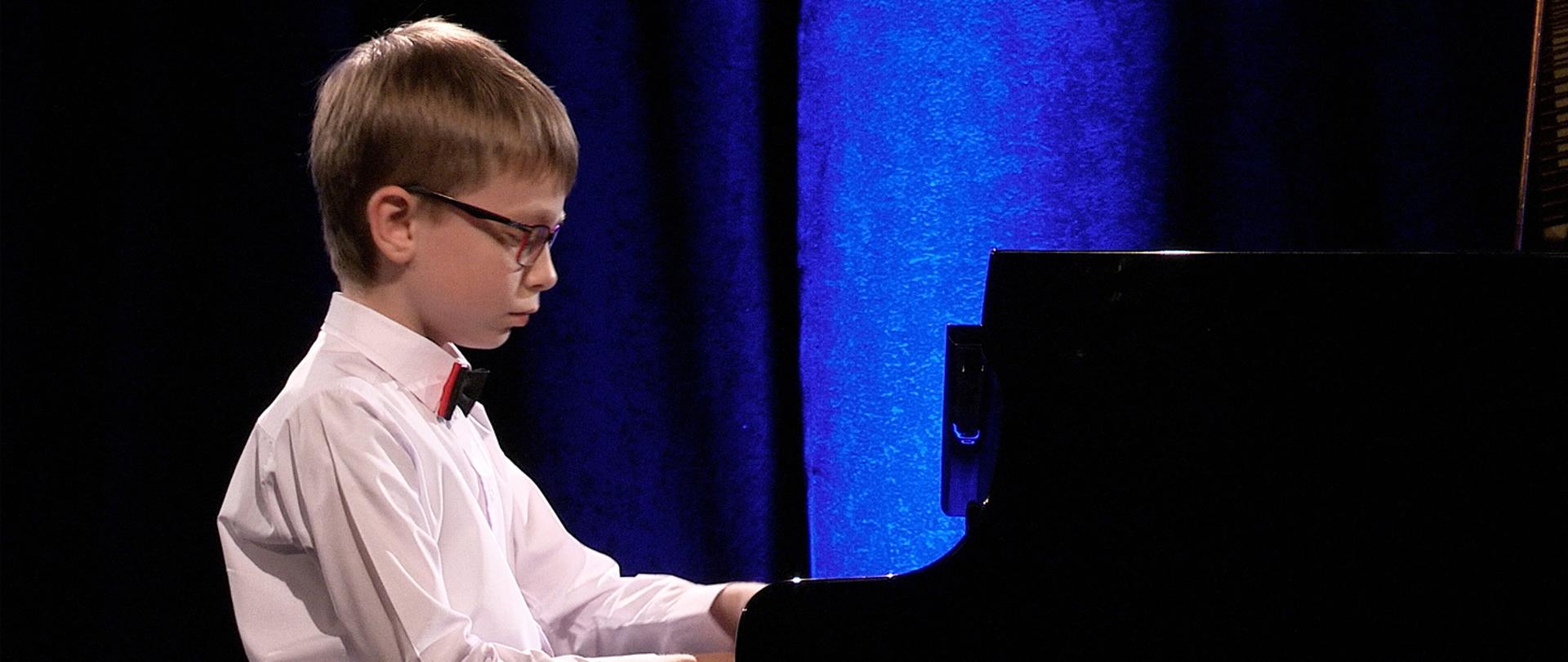 Na zdjęciu widać zbliżenie chłopca grającego na fortepianie. 