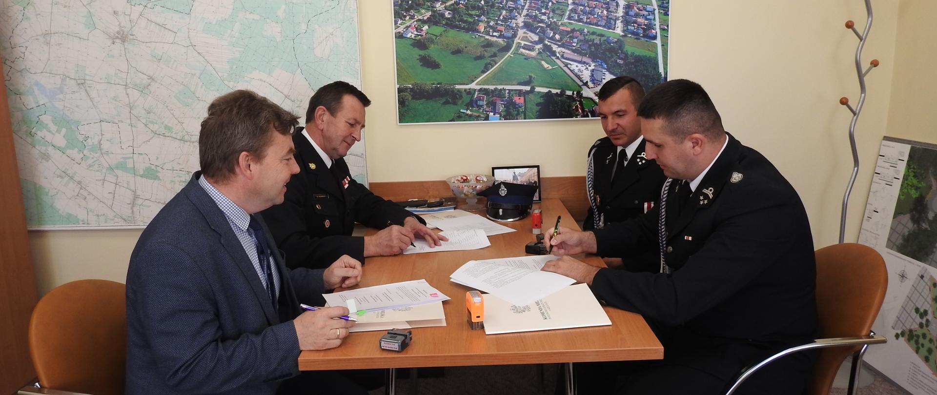 Zdjęcie przedstawia burmistrza miasta i gminy Pierzchnica, komendanta miejskiego PSP w Kielcach oraz przedstawicieli jednostki OSP Pierzchnica w trakcie podpisywania porozumienia. W tle na ścianie widnieje mapa gminy Pierzchnica.