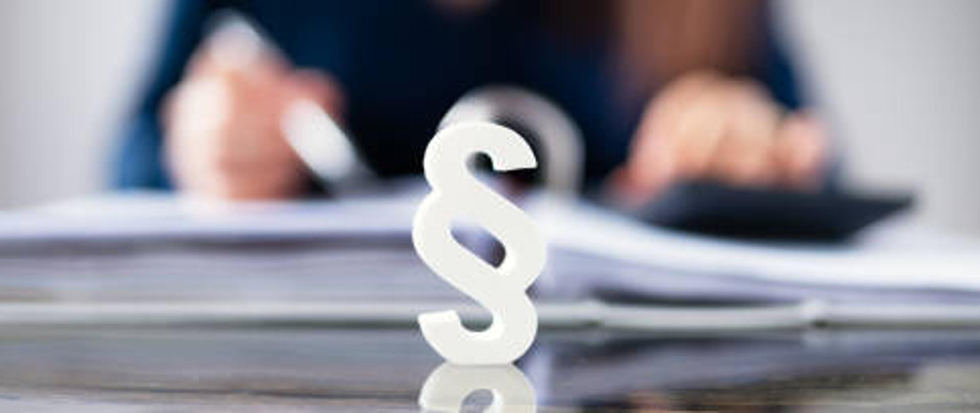 symbol paragrafu, w tle osoba podpisująca dokument