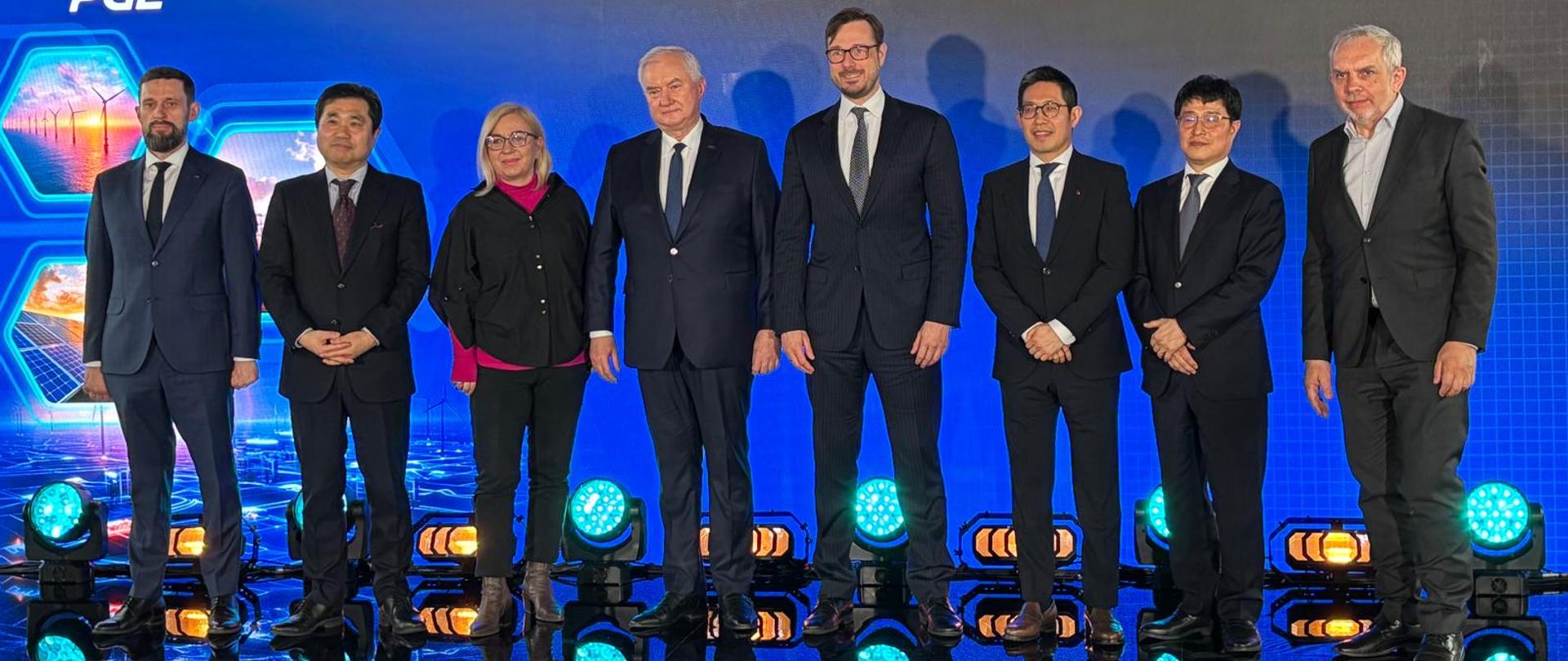 Minister Jakub Jaworowski i inni uczestnicy wydarzenia stoją na tle ścianki z napisem "Elastyczność = Bezpieczeństwo" oraz logotyp PGE. 