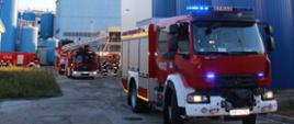 Samochody ratowniczo-gaśnicze biorące udział w działaniach gaśniczych na tle budynków zakładu mleczarskiego.