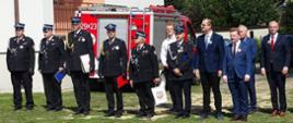Na zdjęciu w szeregu stoją strażacy OCP oraz PSP, a także zaproszeni goście. Za zgromadzonymi znajduje się samochód ratowniczo-gaśniczy oraz drzewa.