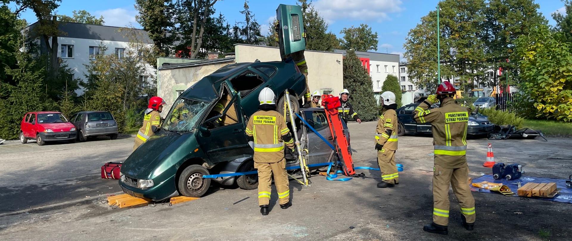 Na placu ćwiczebnym dwa samochody osobowe po wypadku. Wokoło obu pojazdów widoczni strażacy oraz sprzęt ratowniczy. 