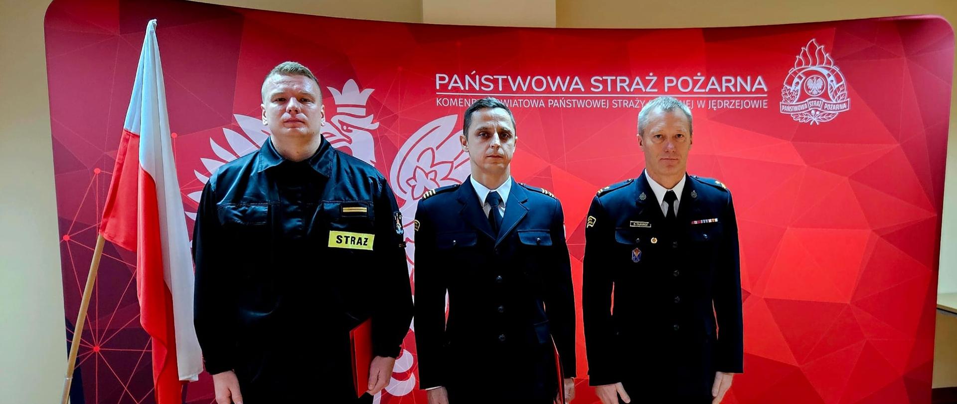Zdjęcie przedstawia awansowanych strażaków w umundurowaniu wyjściowym w asyście komendanta powiatowego Państwowej Straży Pożarnej w Jędrzejowie, st. bryg. Sebastiana Dudzicza.
