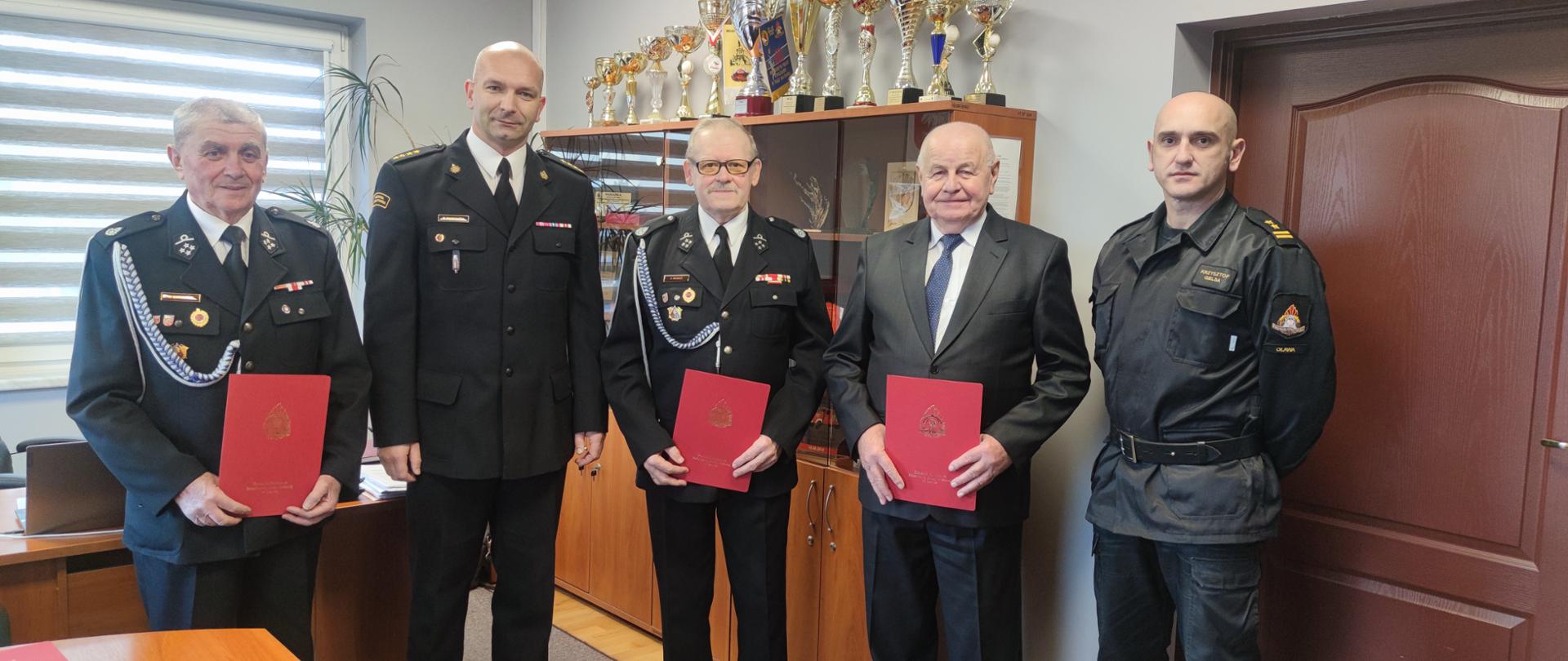 na zdjęciu widać strażaków ochotników, którzy otrzymali dokumenty z decyzjami przyznającymi świadczenie ratownicze. Wraz z nimi stoją: komendant powiatowy i jego zastępca