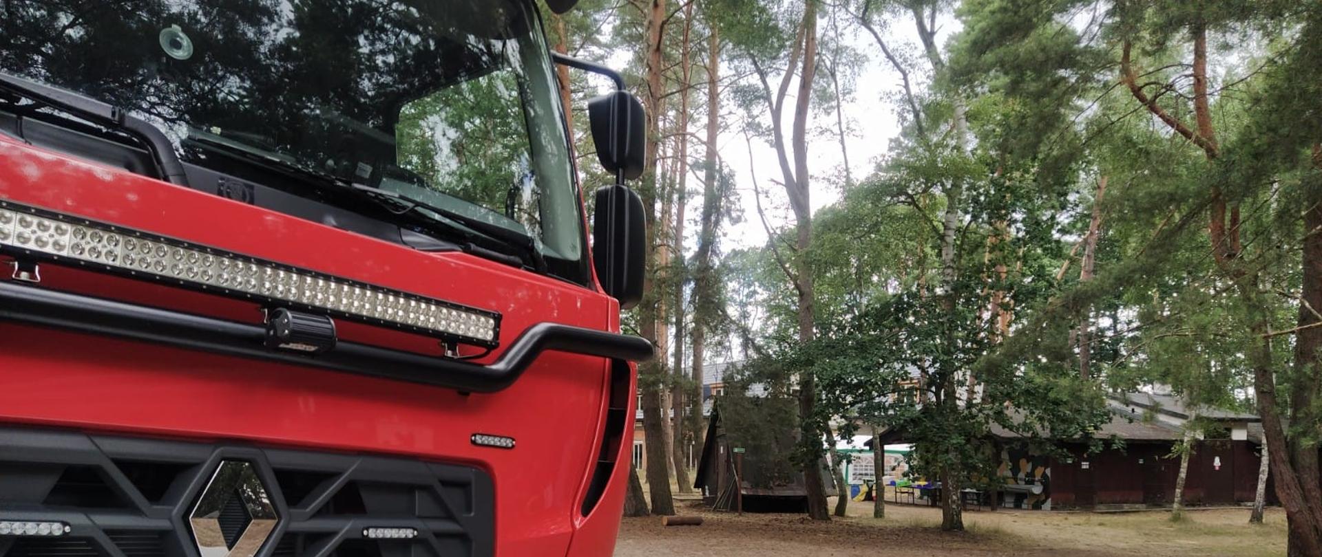 Widok obozu harcerskiego. Na pierwszym planie wóz bojowy straży pożarnej. W tle namioty obozowe i las.