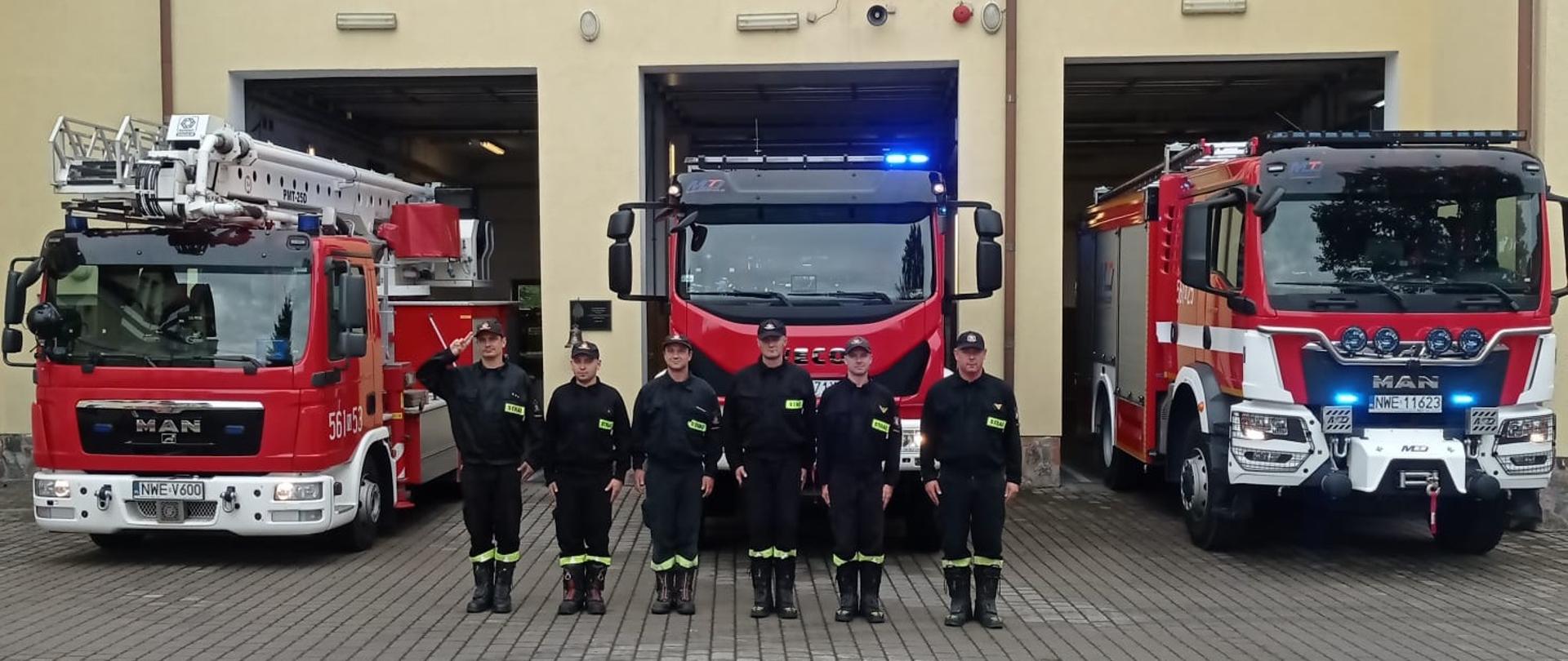 Strażacy stoją przed budynkiem KP za nimi stoją pojazdy. Strażacy oddają honor 