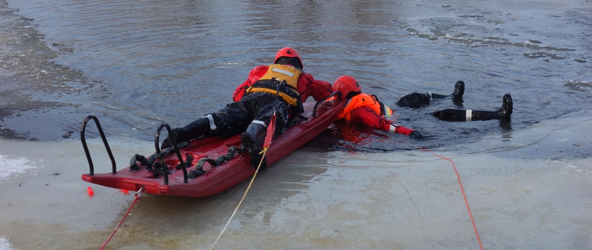 Ćwiczenia wodno - lodowe JRG Końskie. Jeden strażak na saniach lodowych wyciąga drugiego z wody pod którym załamał się lód.