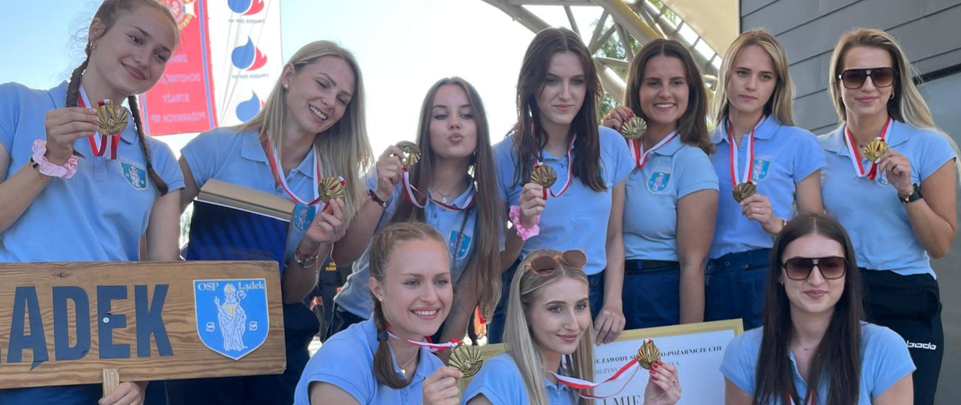 na scenie - zdjęcie grupowe zawdodncizek zkobiecej drużyny pożarniczej z Lądku, kobiety ubrane w niebieskie polówki pokazują medal