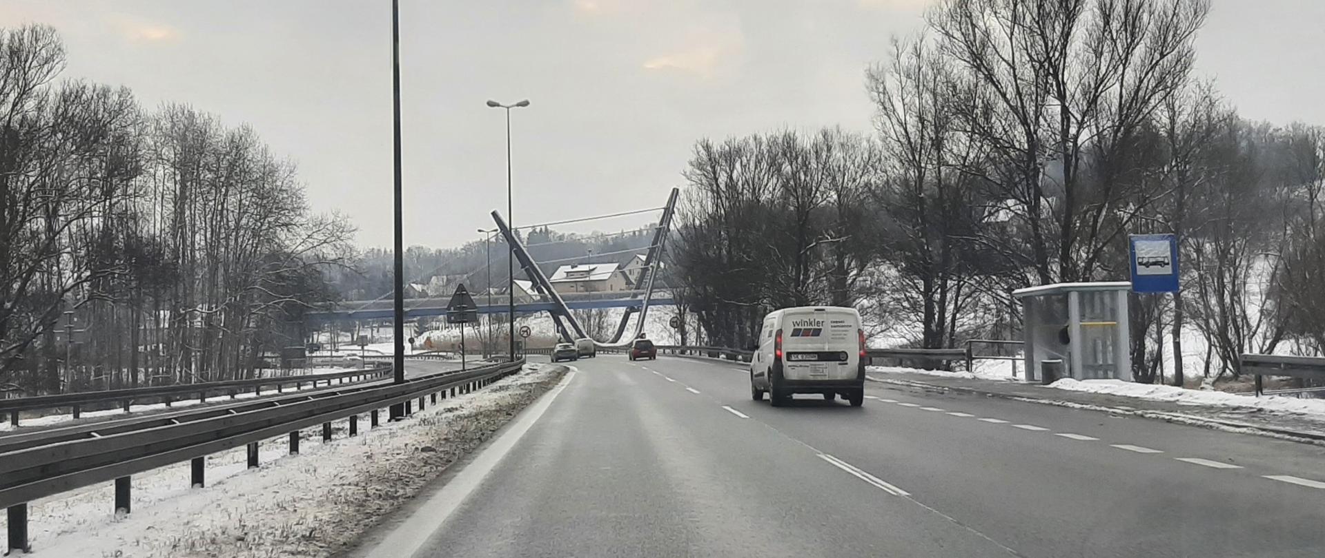droga, jedzie samochód, widzimy jego tył na wprost kładka dla pieszych