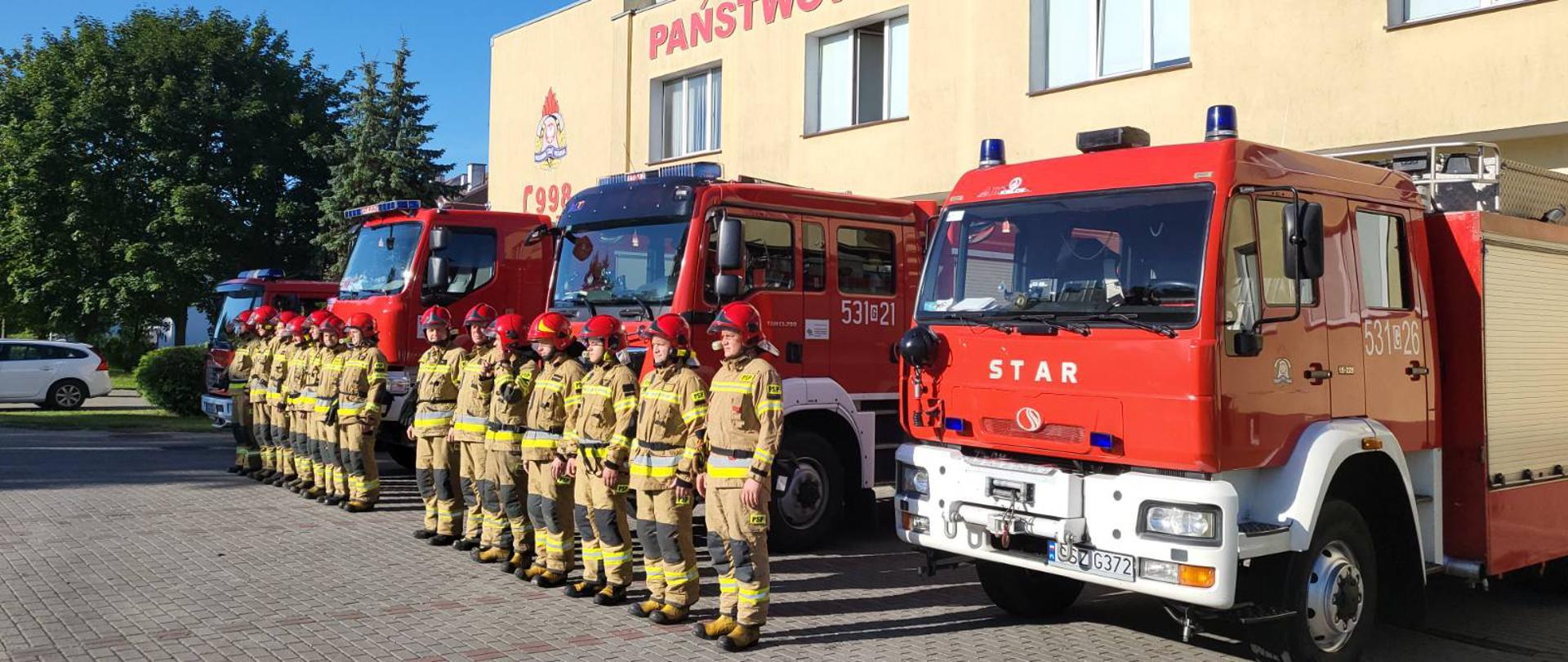 przed strażnicą ustawione wozy z włączonymi sygnałami dźwięowymi i świetlnymi, a przed nimi ustawione dwie zmiany służbowe.