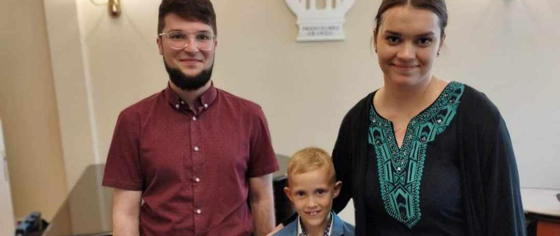 Leon Franas oraz pani Sara Powaga i pan Krystian Klej. Zdjęcie wykonane w auli szkoły.