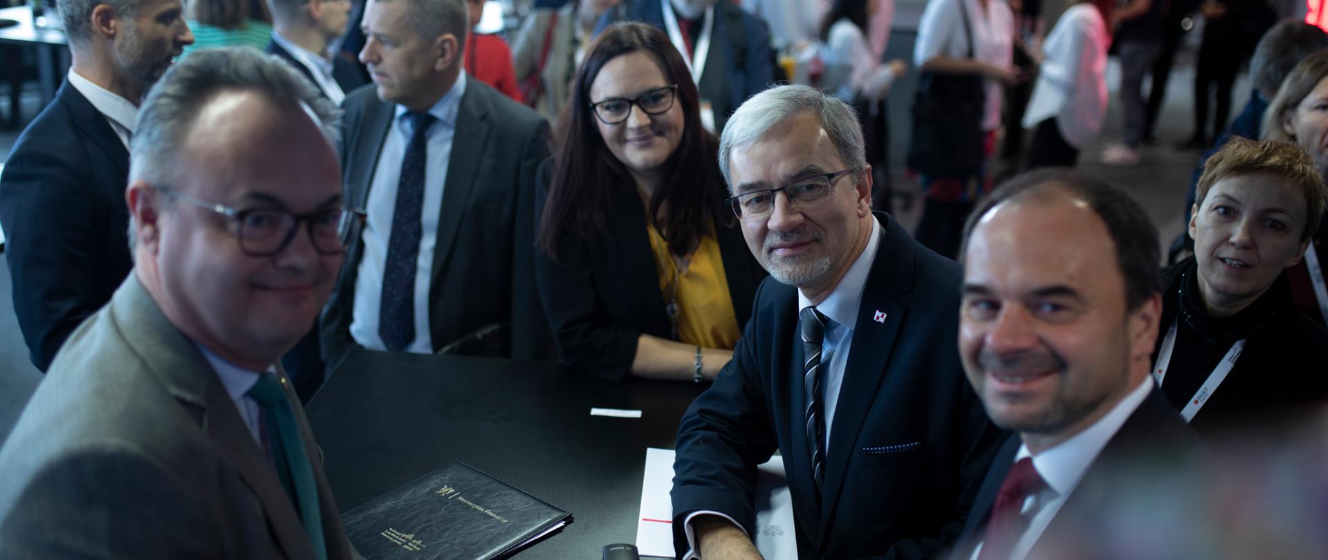 Minister Kwieciński, minister Jarosińska-Jedynak i ambasador Norwegii ‎Olav Myklebust stoją przy stoliku koktajlowym. 