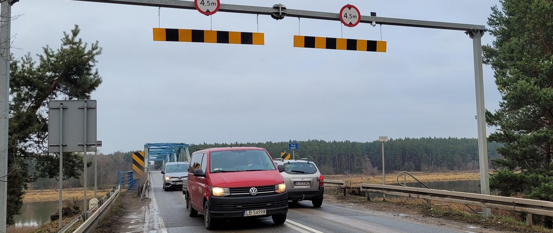 Dojazd do mostu, , po bokach rzeka, na pierwszym planie dwa auta jadące w przeciwnych kierunkach 