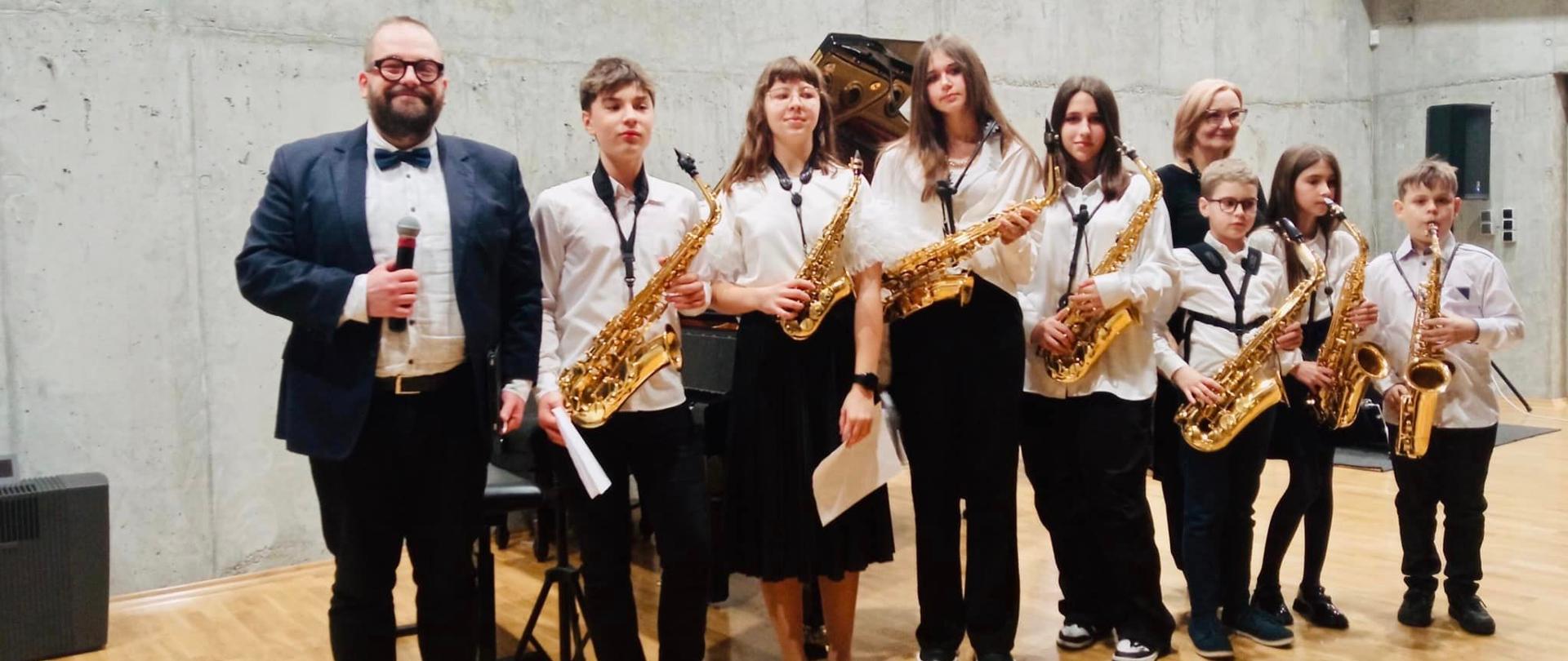 Grupa saksofonistów razem z nauczycielem na scenie sali koncertowej