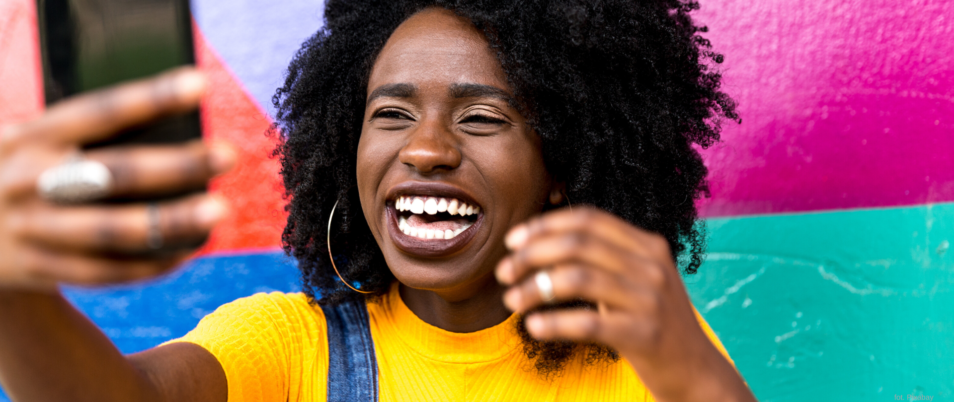 Czarnoskóra, uśmiechnięta kobieta trzymająca telefon komórkowy