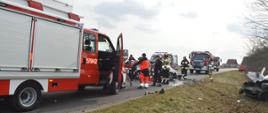 Zderzenie dwóch aut. Okolice Zaborowic. Odcinek jezdni, na którym doszło do wypadku. Na pierwszym planie wóz straży pożarnej przodem zwrócony w stronę wioski. Przed nim volkswagen golf uczestniczący w wypadku. Za nim z kolei dwa wozy strażackie i karetka pogotowia ratunkowego . Wokół rozbitego samochodu znajdują się strażacy i ratownicy medyczni. W tle zabudowania.