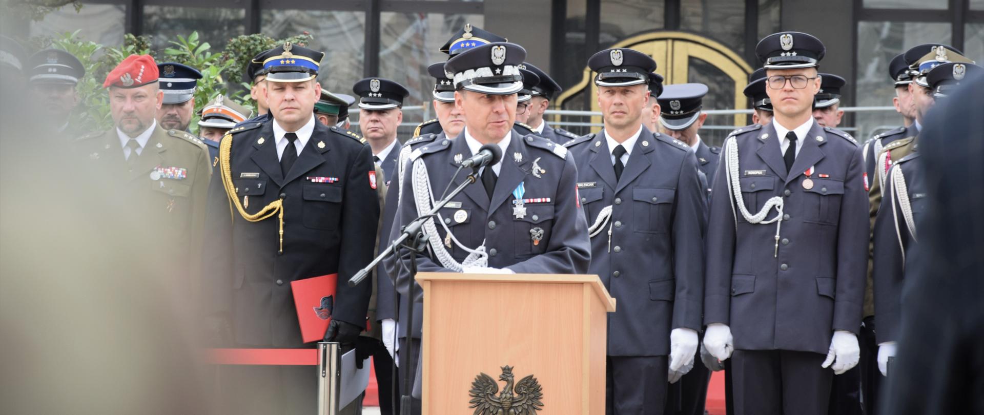 Zdjęcie przedstawia zaproszonych gości ustawionych na trybunie honorowej. Przy mównicy głos zabiera Generał. W tle pozostali zaproszeni goście.