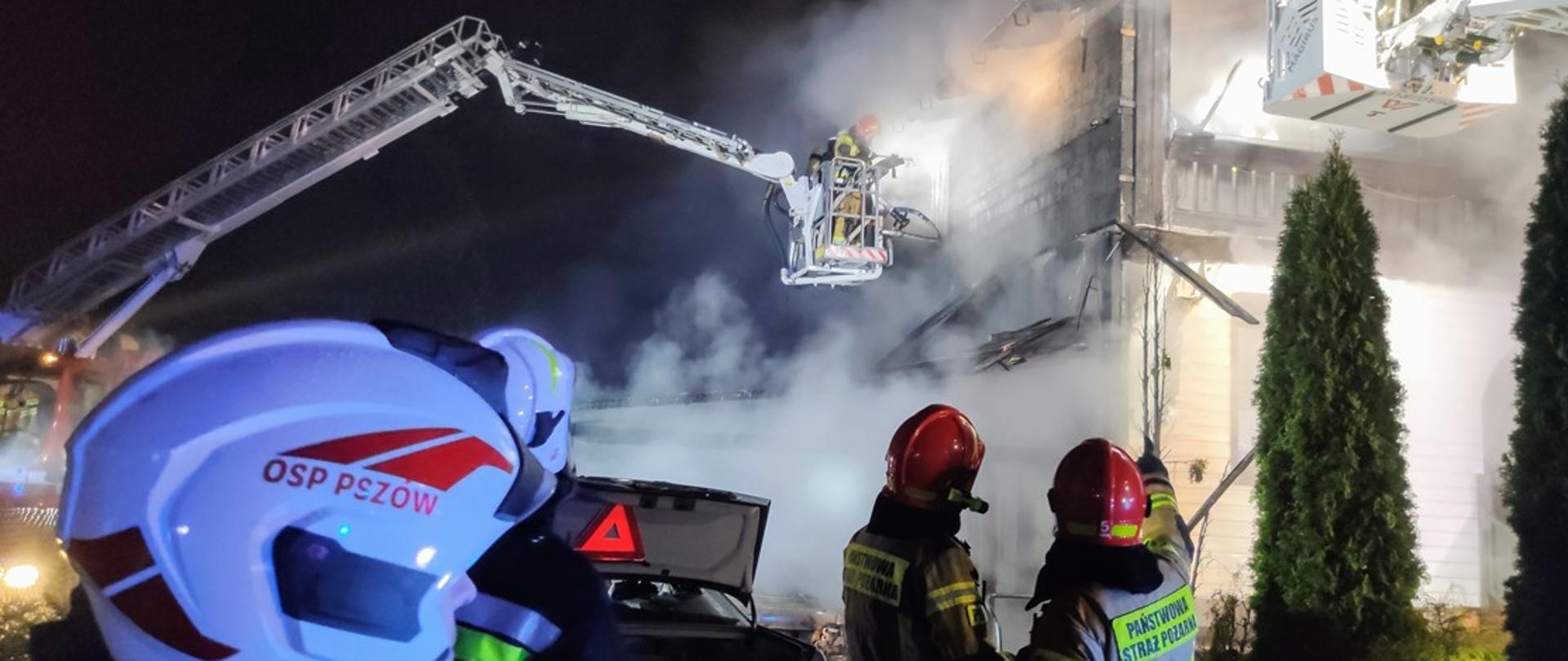 Na zdjęciu czterech strażaków na tle zadymionego budynku. 