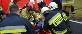 Zderzenie pojazdów. Droga krajowa nr 36 (Dłoń-Smolice). Na jezdni strażacy udzielają kwalifikowanej pierwszej pomocy poszkodowanej uczestniczce kolizji. Korzystają z zestawu ratownictwa medycznego PSP R1. W tle stoi parawan ochronny koloru czerwonego. 