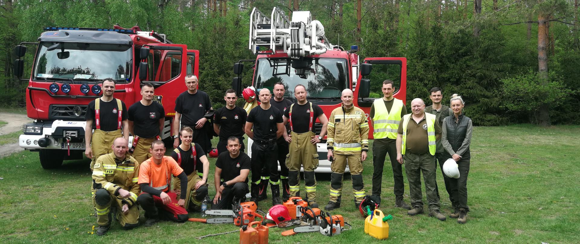 Wspólne zdjęcie strażaków oraz prowadzących ćwiczenia na tle samochodów pożarniczych.