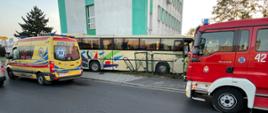 Na zdjęciu widać samochód strażacki oraz karetkę pogotowia, w tle widać budynek w który uderzył autobus