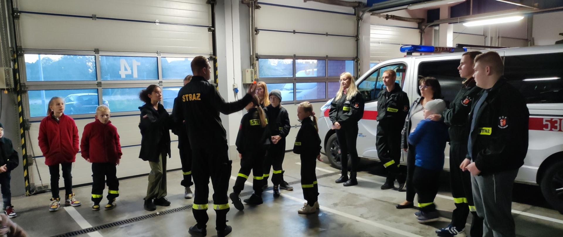 Funkcjonariusz PSP oprowadza MDP po strażnicy w tle samochód strażacki