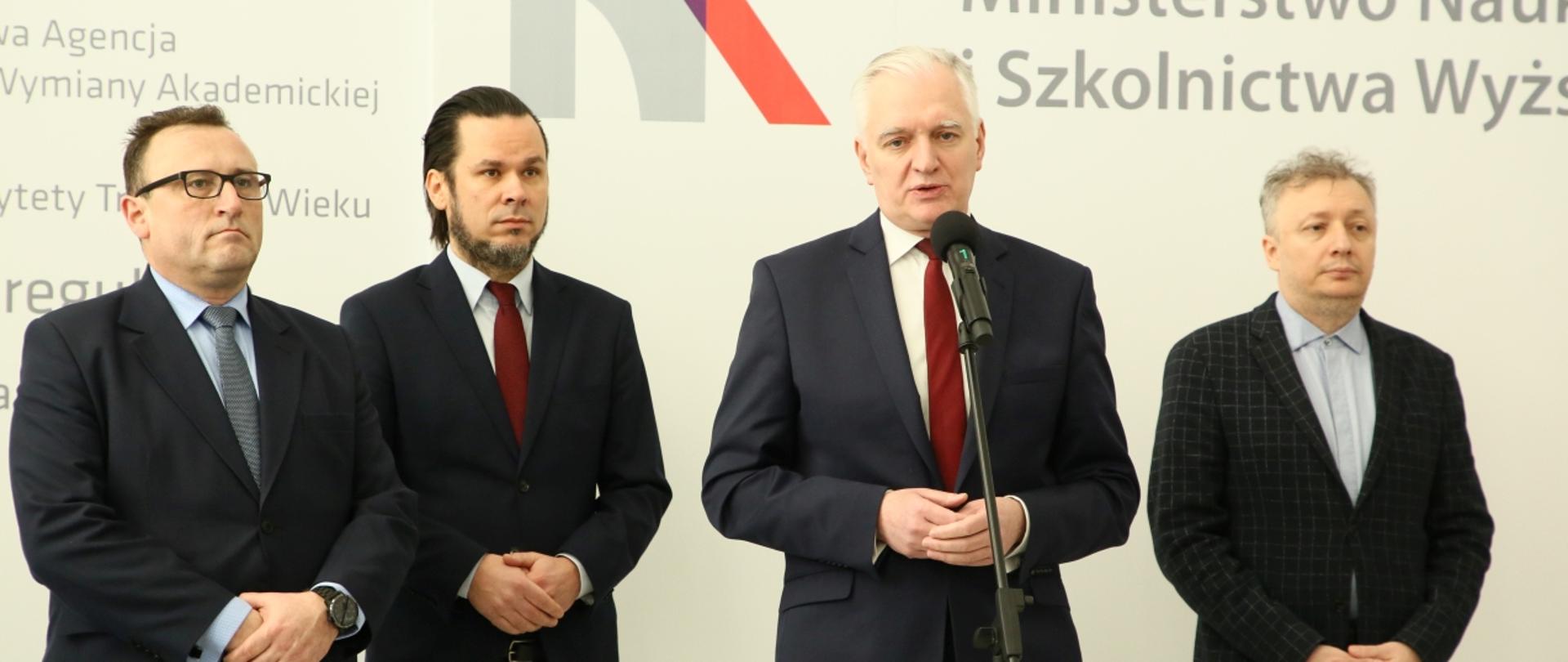 Minister Gowin, wiceminister Skuza i rektorzy uczelni stoją na tle ściany z logiem MNiSW