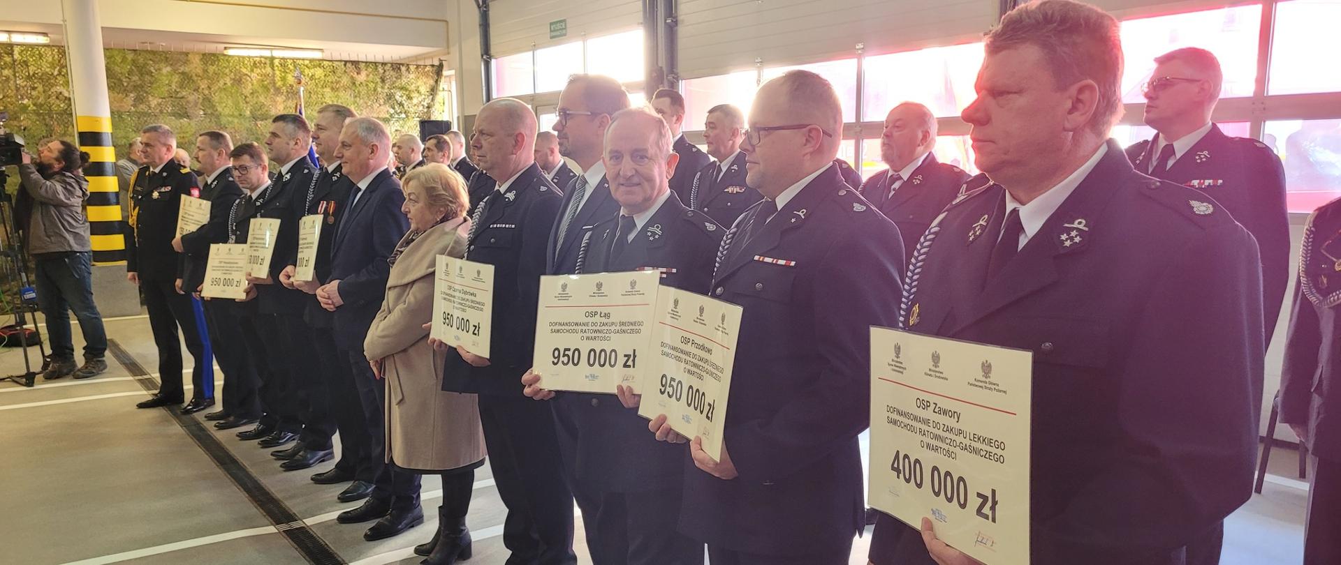 Druhowie OSP pozują do zdjęcia z promesami w towarzystwie Wojewody Pomorskiego oraz Pomorskiego Komendanta Wojewódzkiego PSP.