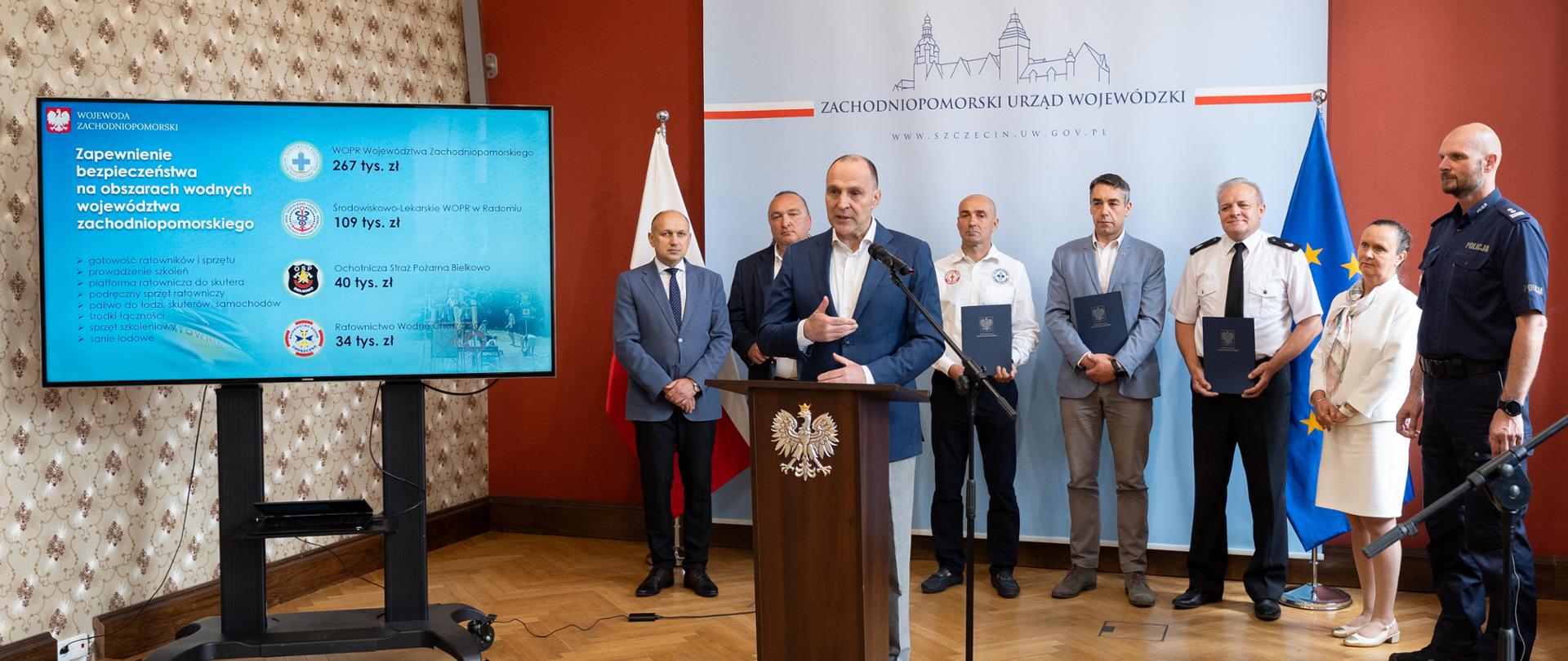 wojewoda przy mównicy, w tle uczestnicy konferencji - szefowie służb i stowarzyszeń odpowiedzialnych za bezpieczeństwo w czasie wakacji