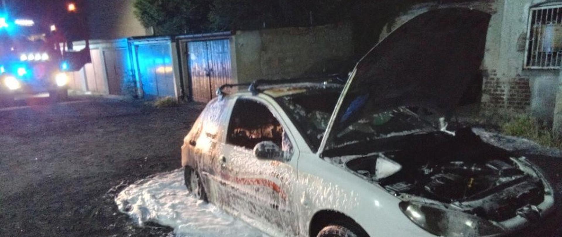 Spalony wrak samochodu w nocy, pokryty pianą gaśniczą.