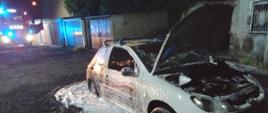 Spalony wrak samochodu w nocy, pokryty pianą gaśniczą.