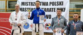 Zdjęcie przedstawia zawodników Karate w strojach sportowych. Na najwyższym stopniu podium stoi krotoszyński strażak.
