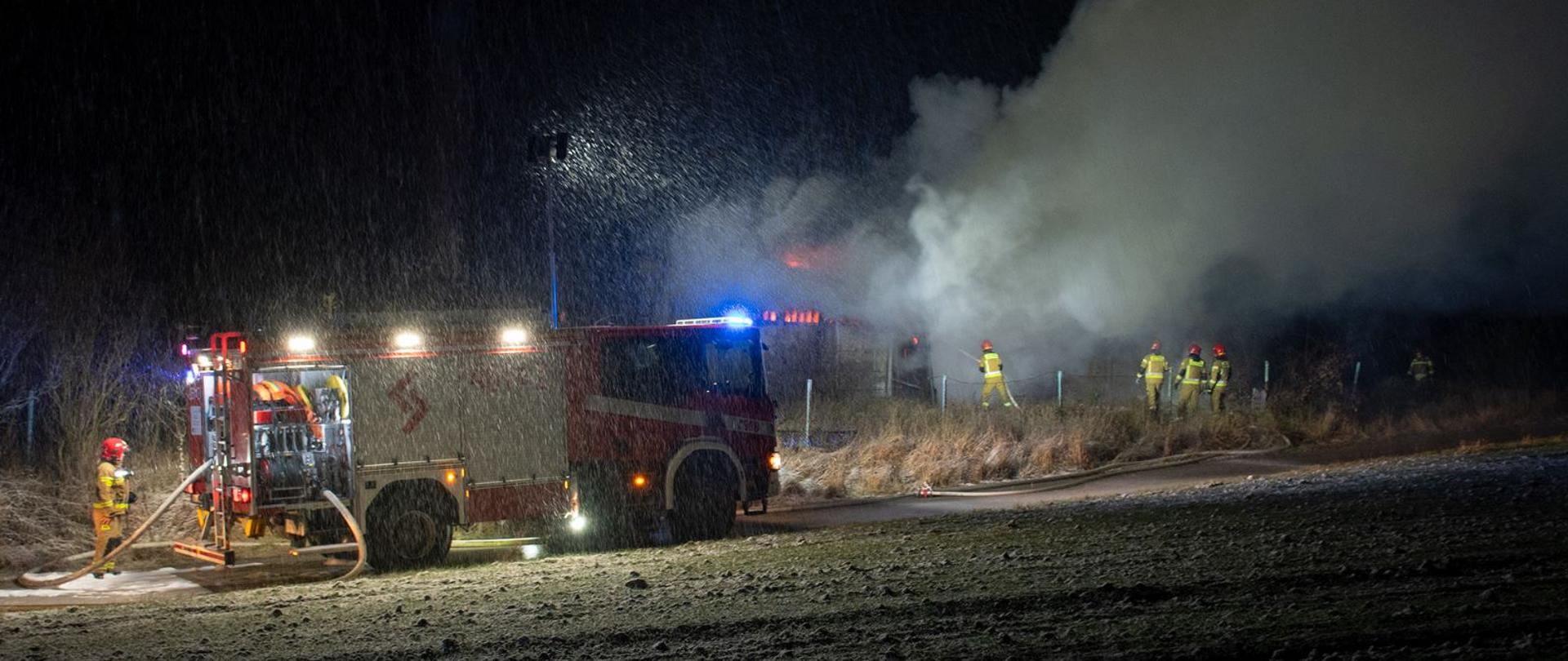 Na zdjęciu widoczny samochód pożarniczy oraz strażaków gaszących pożar balotów słomy w warunkach zimowych