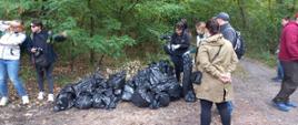 Sterta worków ze śmieciami w lesie i kilka osób, które właśnie skończyły sprzątać 
