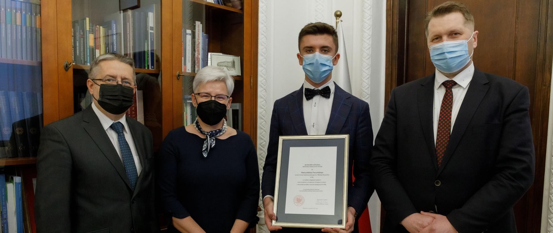 Spotkanie Ministra Edukacji i Nauki z Maksymilianem Paczyńskim - uczniem Liceum Ogólnokształcącego im. Mikołaja Kopernika w Iłży - zwycięzcą światowego konkursu Impact Creators, minister Przemysław Czarnek siedzi przy stole podczas spotkania z Maksymilianem Paczyńskim, minister Przemysław Czarnek stoi wraz z Maksymilianem Paczyńskim. Maksymilian Paczyński trzyma dyplom uznania.