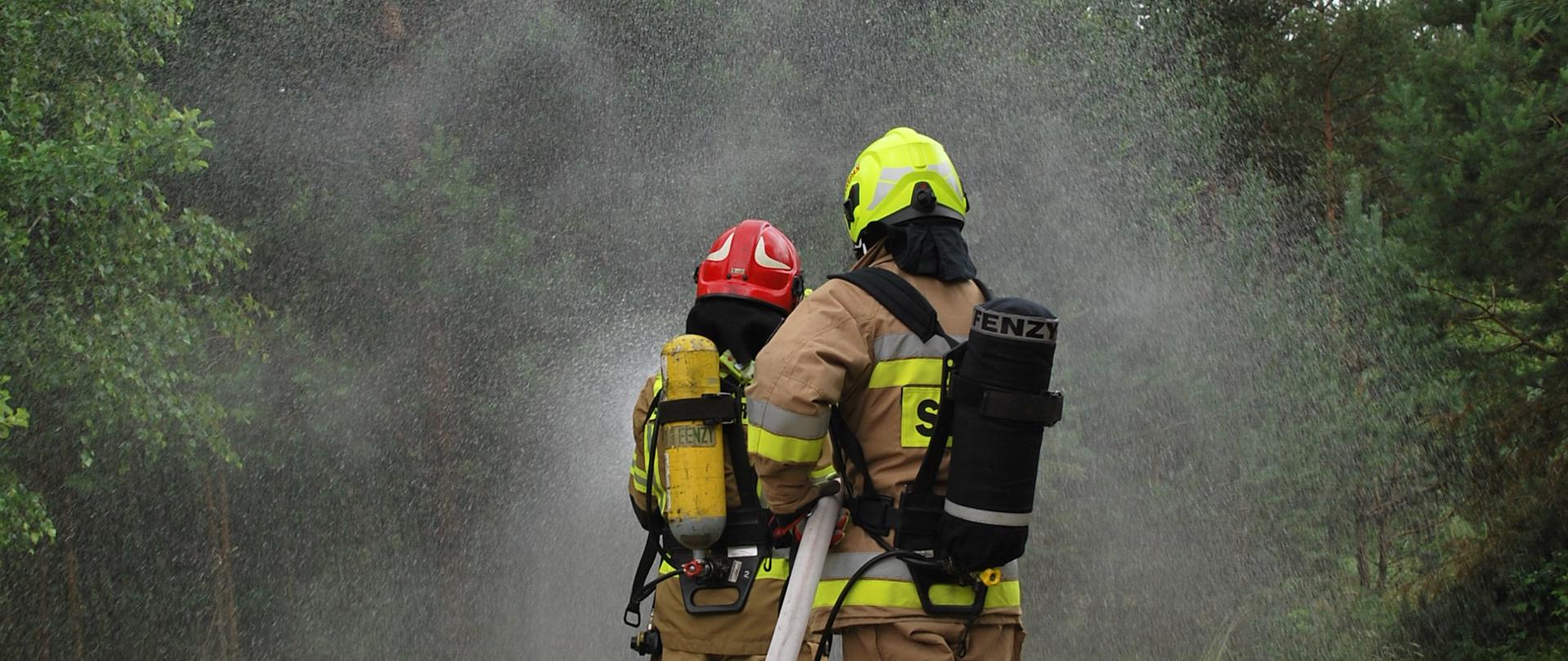 Na zdjęciu dwóch strażaków w ubraniu specjalnym podaje prąd wody w natarciu