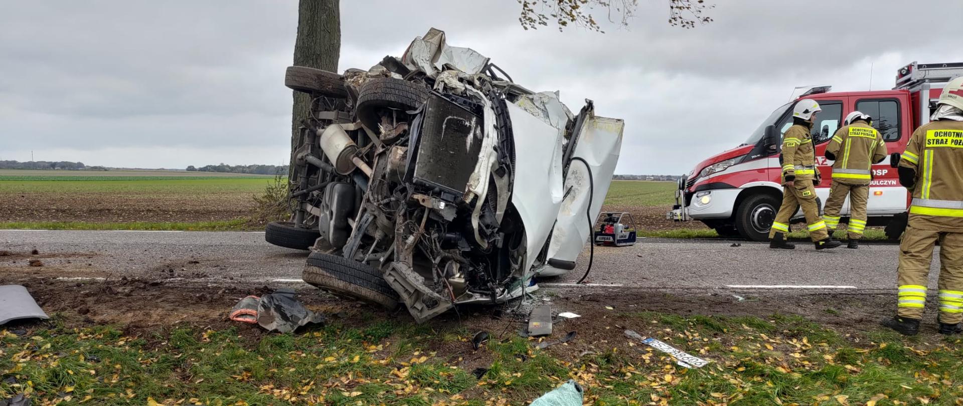 Uszkodzony samochód na drodze, po prawej strażacy