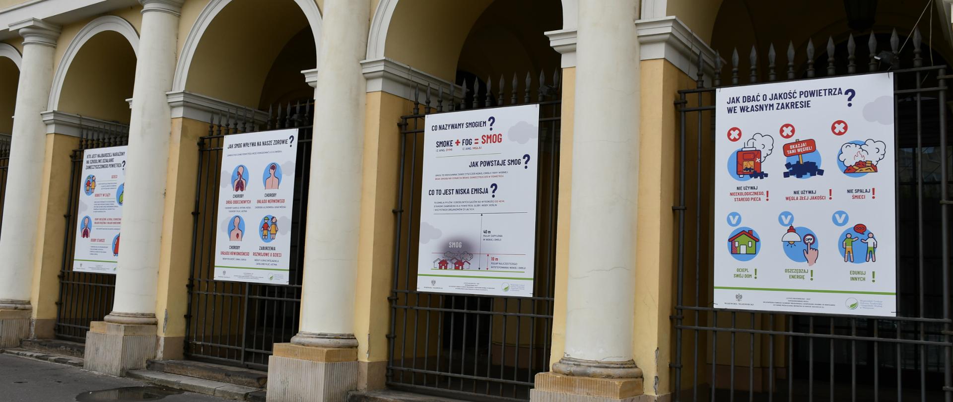 Na zdjęciu znajdują się cztery plakaty, stanowiące wystawę plenerową, która w czytelny sposób przekazuje podstawowe informacje o zanieczyszczeniu powietrza i możliwościach niwelacji zagrożenia. Wystawa umieszczona jest na fragmentach ogrodzeń, wtopionych w arkady budynku Mazowieckiego Urzędu Wojewódzkiego w Warszawie. 