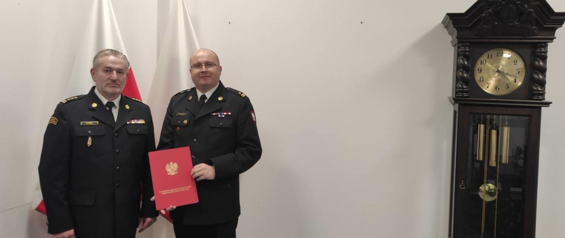Zdjęcie komendanta wojewódzkiego z komendantem miejskim w Sopocie na tle flag oraz zabytkowego zegara