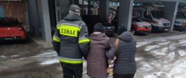 Na zdjęciu widnieje strażak Ochotniczej Straży Pożarnej pomagający przetransportować osobę starszą do punktu szczepień przeciwko COVID-19. 