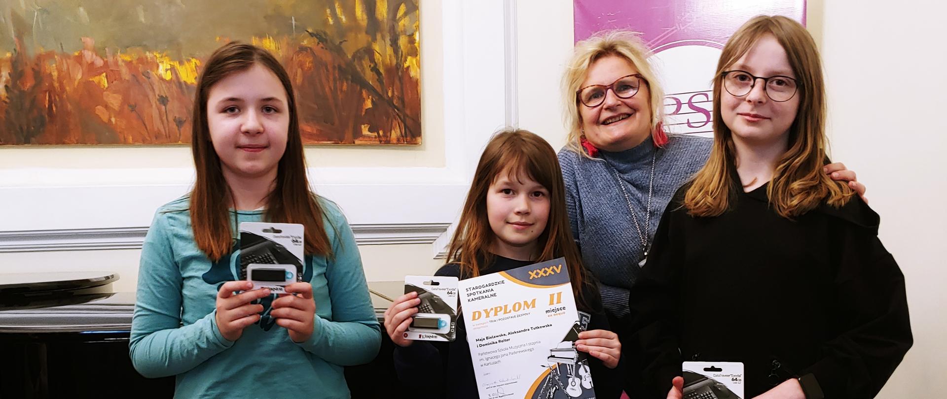 Uczennice trzymające nagrody i dyplom, na drugim planie nauczycielka