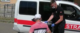 Strażak z OSP Skarżysko-Kamienna pomaga mężczyźnie na wózku dostać się na szczepienie.