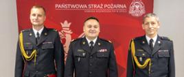 Wspólne zdjęcie nadbryg. Krzysztofa Kędryka Opolskiego Komendanta Wojewódzkiego PSP wraz z mł. bryg. Szymonem Jędrzejasem Zastępcą Komendanta Powiatowego Państwowej Straży Pożarnej w Kędzierzynie-Koźlu oraz mł. bryg. Mariusz Strzelczak Zastępca Komendanta Powiatowego Państwowej Straży Pożarnej w Oleśnie. W tle czerwony banner Państwowej Straży Pożarnej wraz z białym godłem Rzeczypospolitej Polskiej. Strażacy w mundurach galowych i wyjściowym.