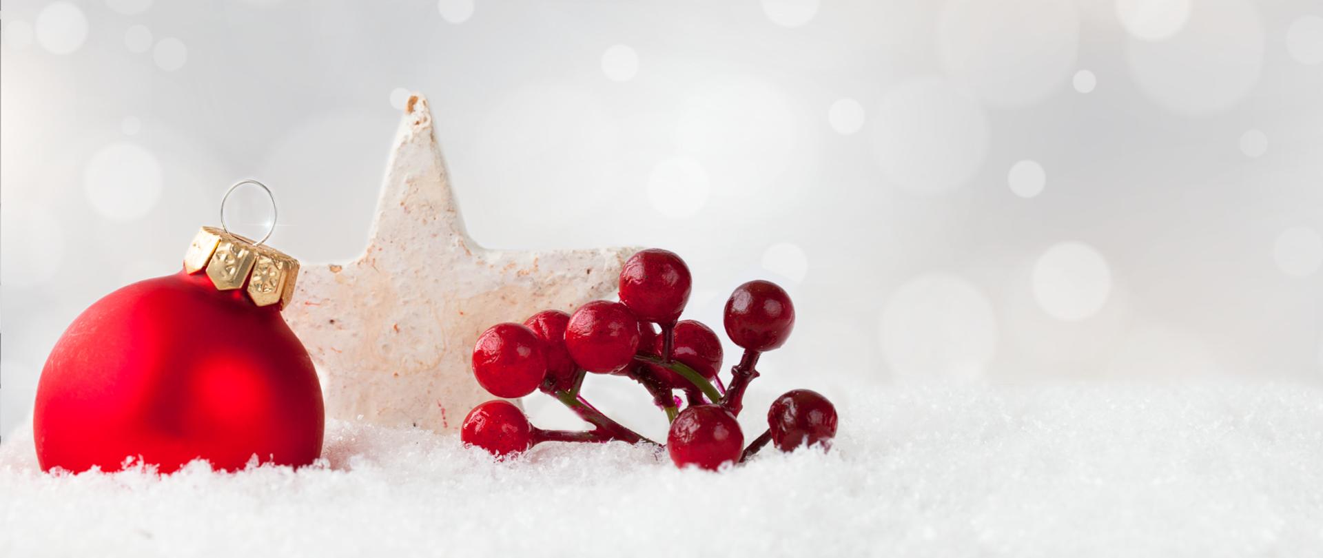 A red Christmas ornament and holly shrub berries, and a white star on a snowy surface