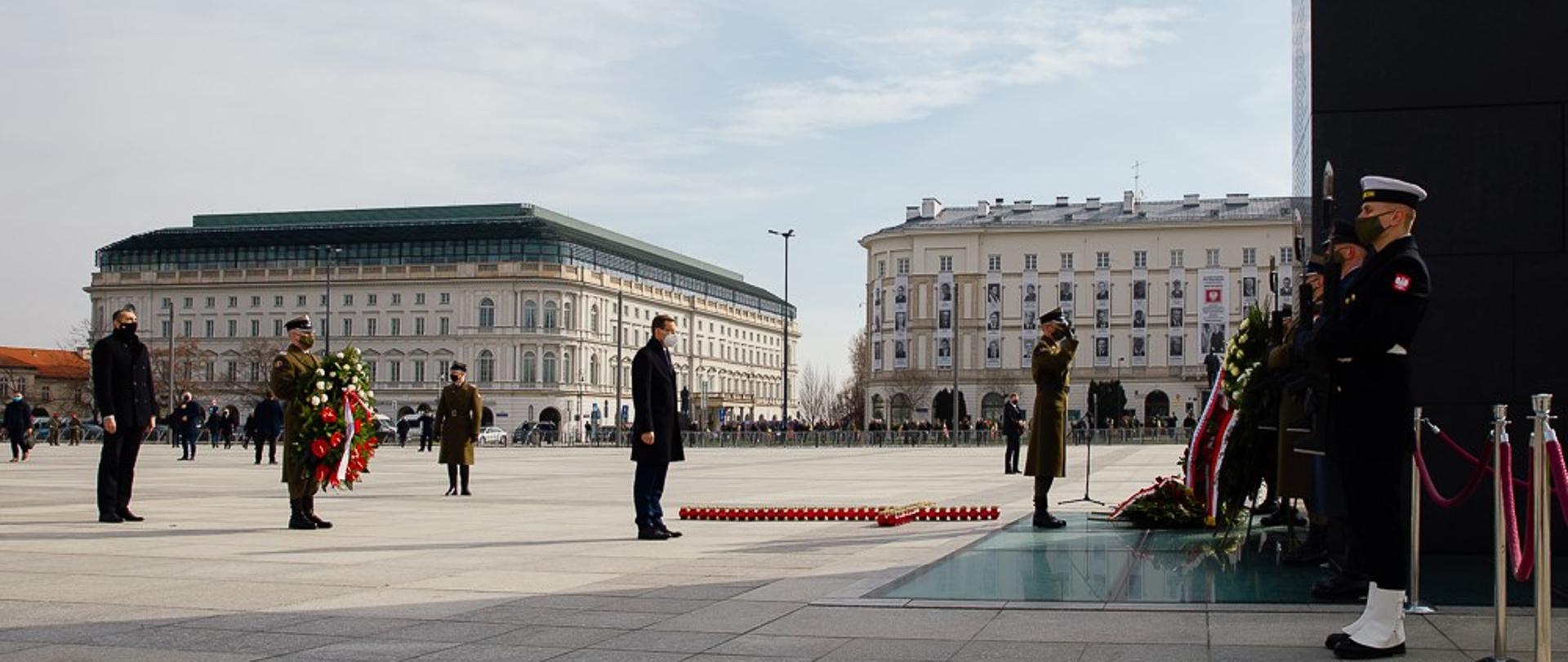 Premier Mateusz Morawiecki stoi z asystą wojskową przed pomnikiem Ofiar Tragedii Smoleńskiej 2010 roku w Warszawie.