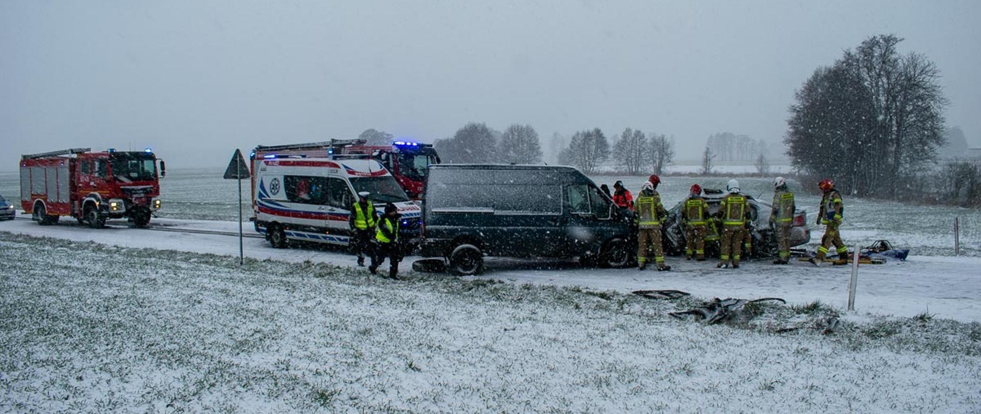 Na zdjęciu czerwone samochody strażackie, samochód policji, karetka pogotowia oraz samochód dostawczy wraz samochodem osobowym biorący udział w zdarzeniu