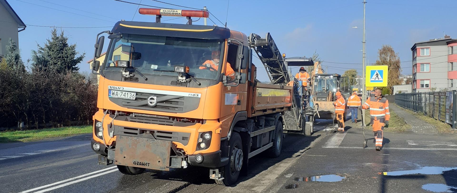 Remont drogi krajowej w Sandomierzu - na jezdni stoi samochód ciężarowy i maszyna do usuwania starej nawierzchni, obok drogowcy pracujący przy remoncie 