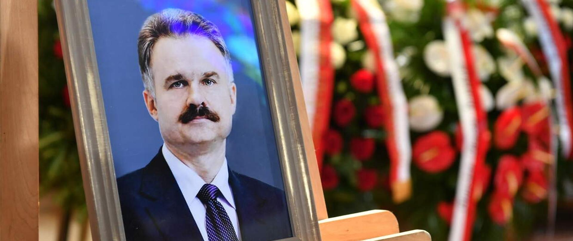 Zdjęcie prof. Waldemara Parucha w ramce. W tle wieńce pogrzebowe z polskimi flagami.