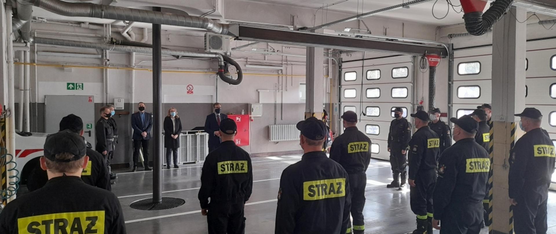 Zbiórka strażaków w garażu jednostki. Przemawia pan poseł Maciej Małecki.